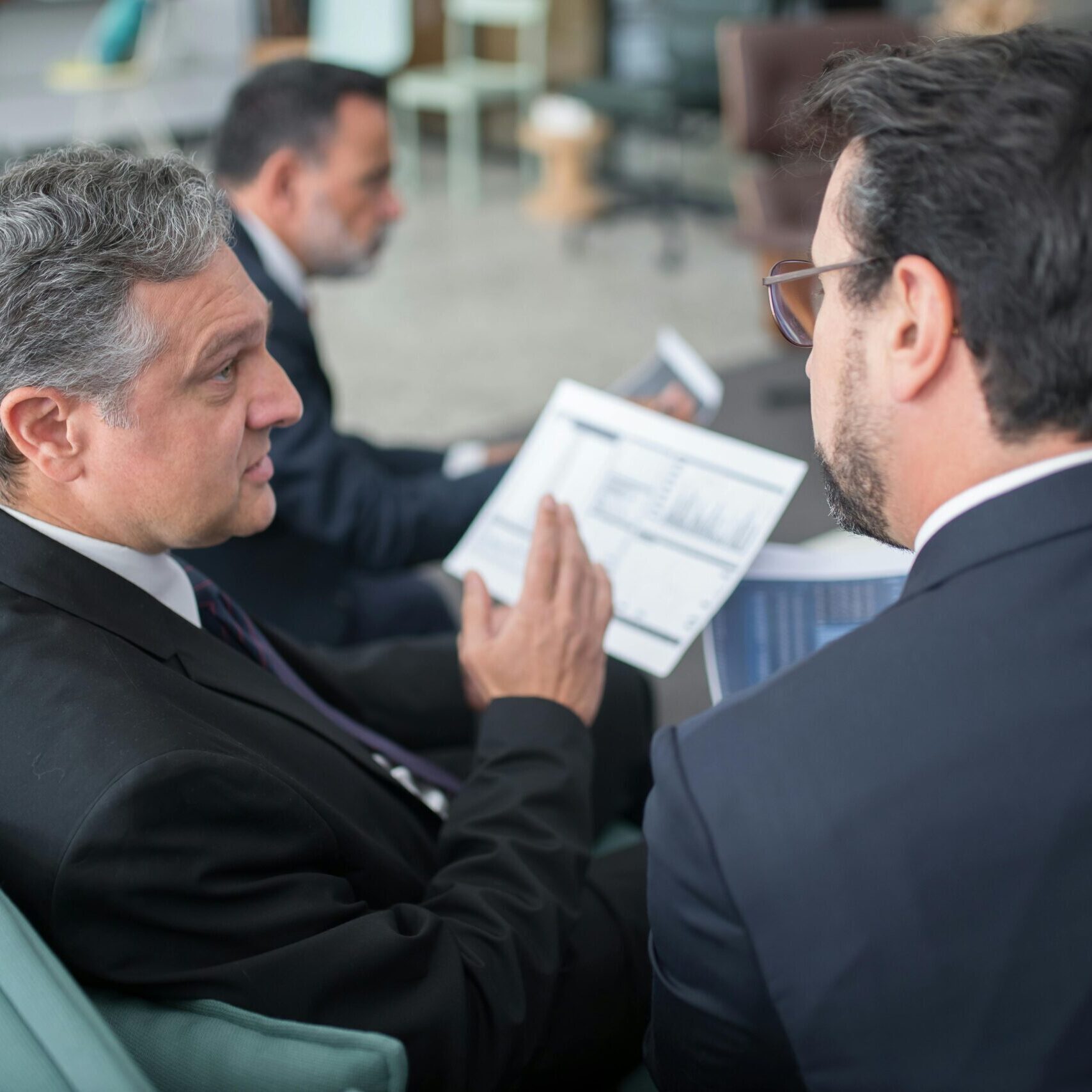 Two businessmen engaged in a discussion, examining reports in a modern office environment.
