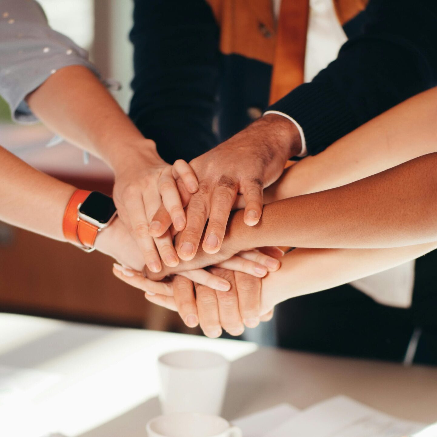 A close-up shot of diverse team members stacking hands over a white table, symbolizing unity and collaboration.